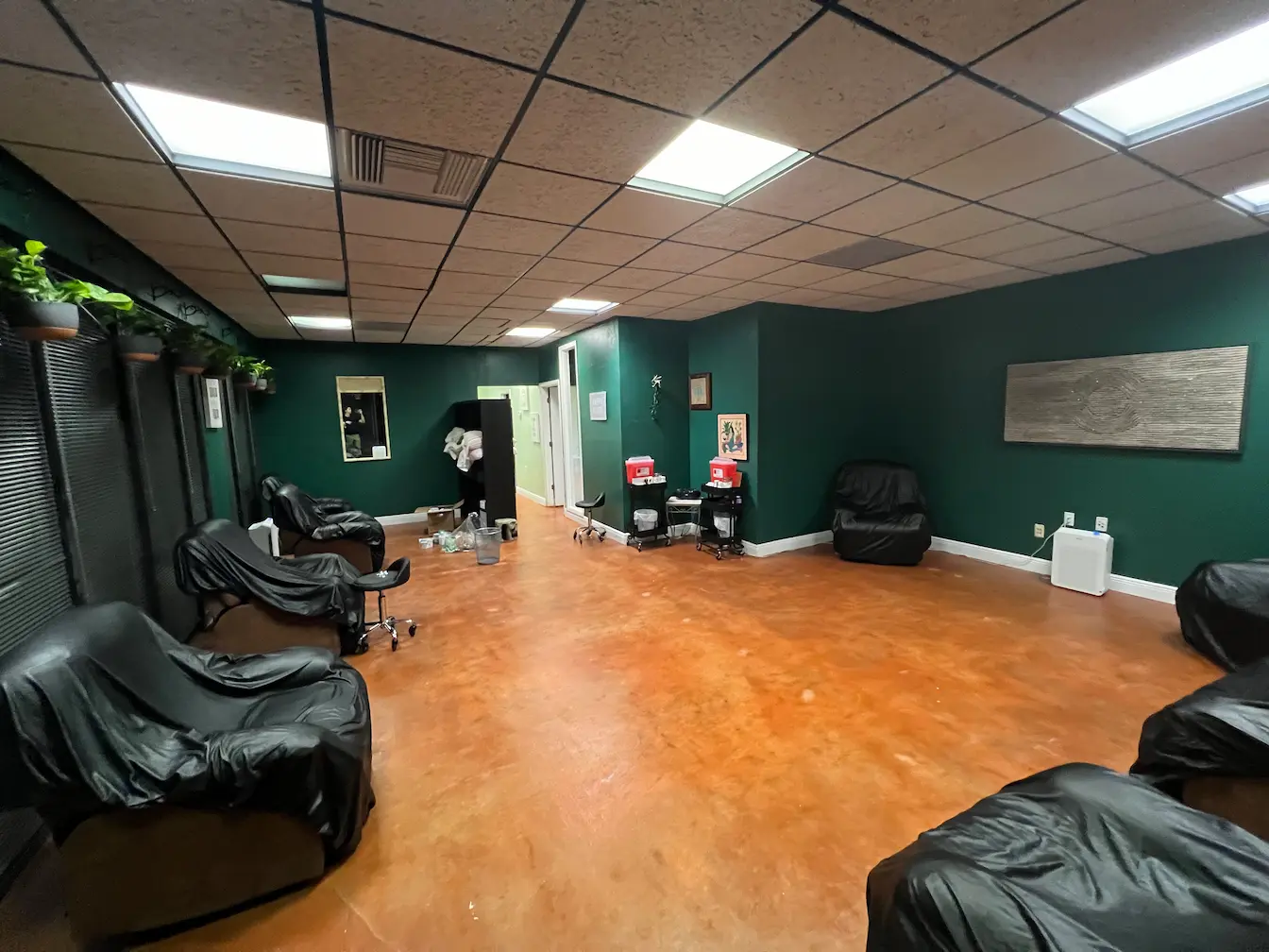 Clnic space, red concrete floor, dark green walls, recliners around the edge with black leather covers